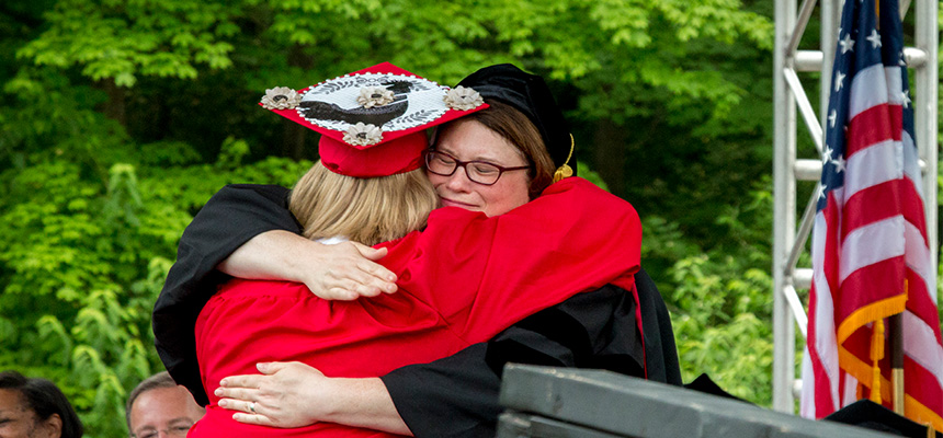 A student hugging their professor on the stage during the divisional recognition ceremony.