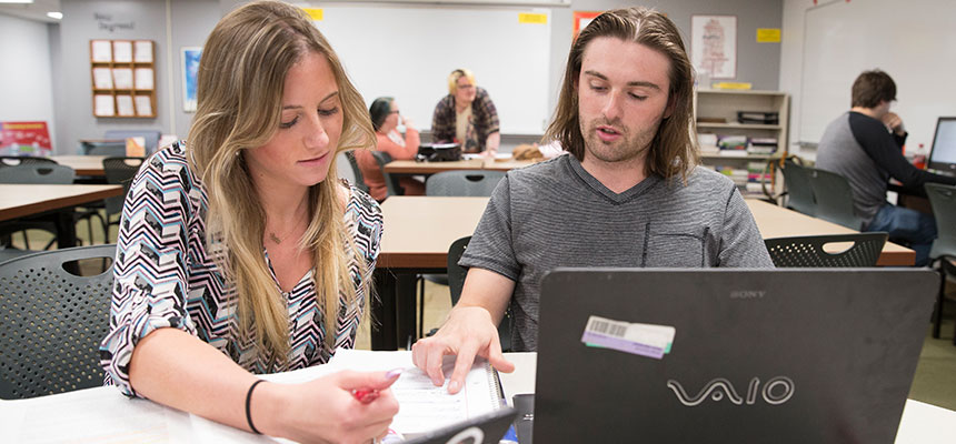 A student being tutored while working on his laptop.