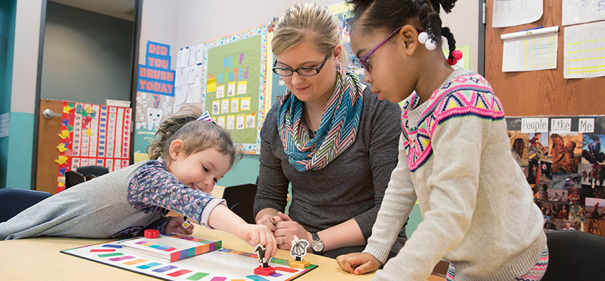 A prek teacher playing a board game with 2 students.
