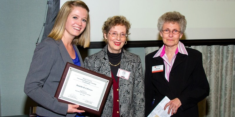 A female student poses with her award next to two women