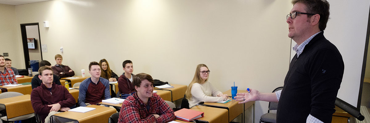 A professor standing in front of the classroom talking to students.
