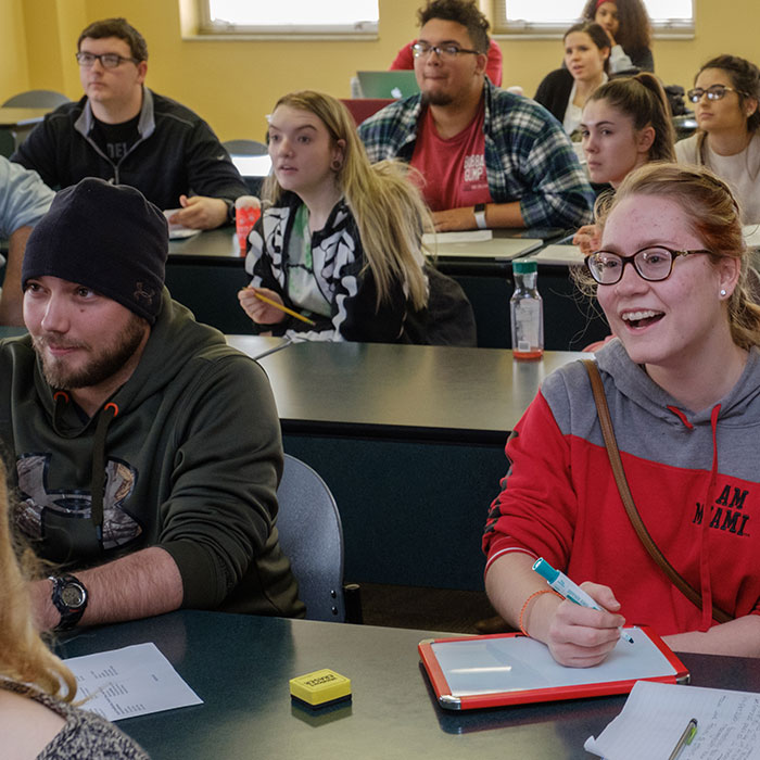 A male and female students sitting at their desks smiling and laughing.
