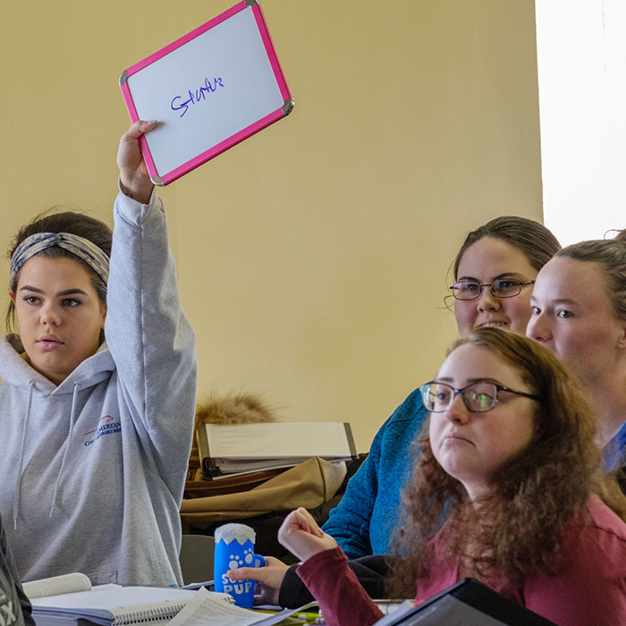 A group of female students sitting around a table with one of them holding up a small whiteboard that reads structure.