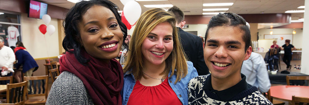 3 students standing with their arms around each other smiling.