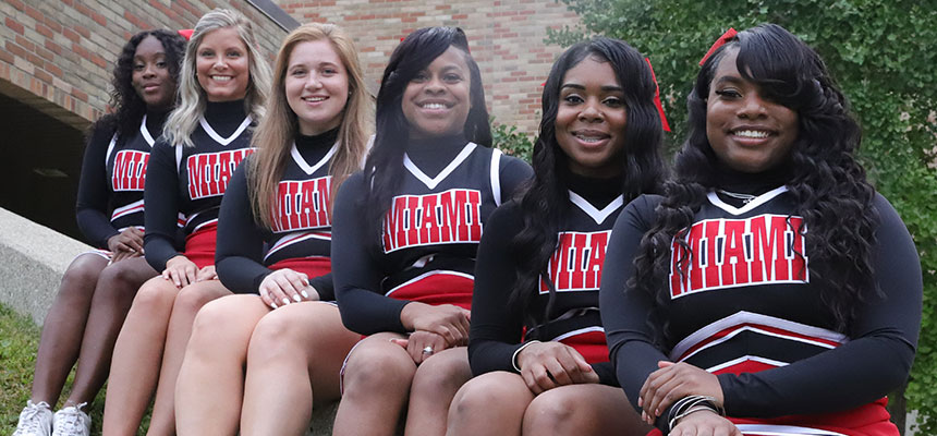 The Miami Hamilton cheerleaders sitting on a concrete ledge in front of the gym