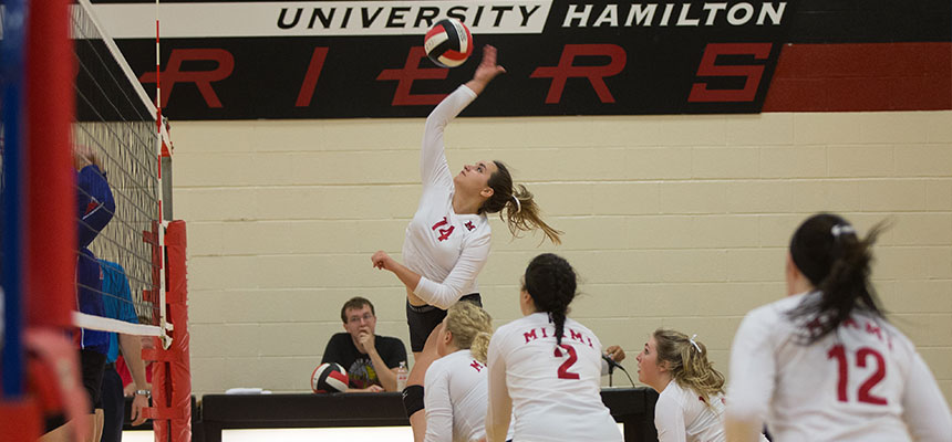 Women's Volleyball player jumping in the air to spike the ball over the net to her opponent.
