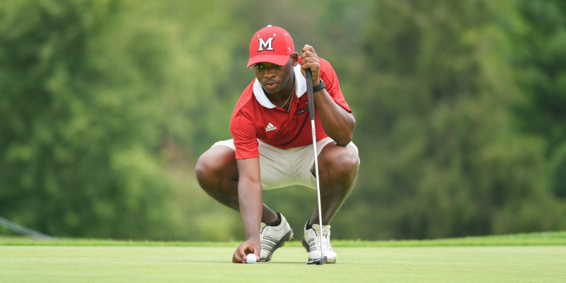 Men's golfer squatting on the green reading his putt.