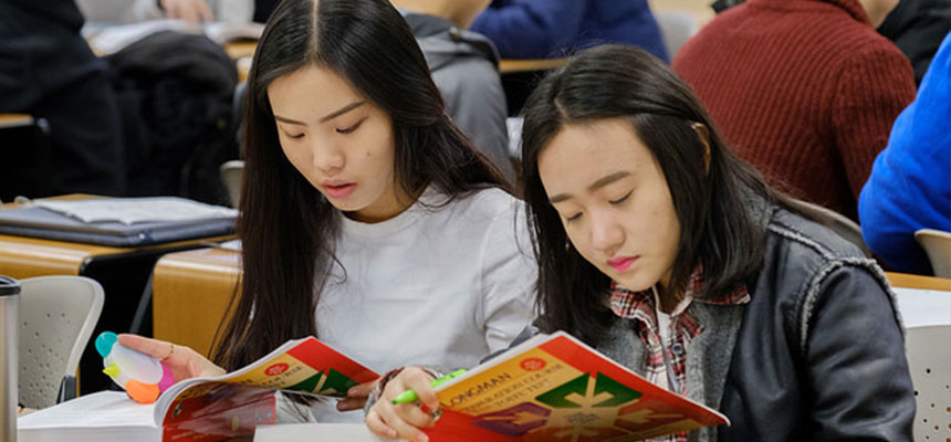 2 female international students sitting at their desks reading their books
