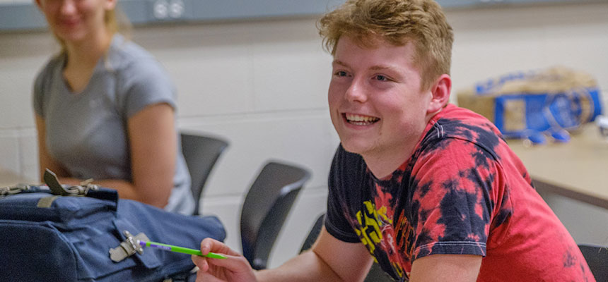A male student sitting at his desk smiling.