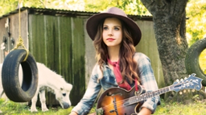 Sierra Hull sitting on the ground with her guitar and a horse in the background