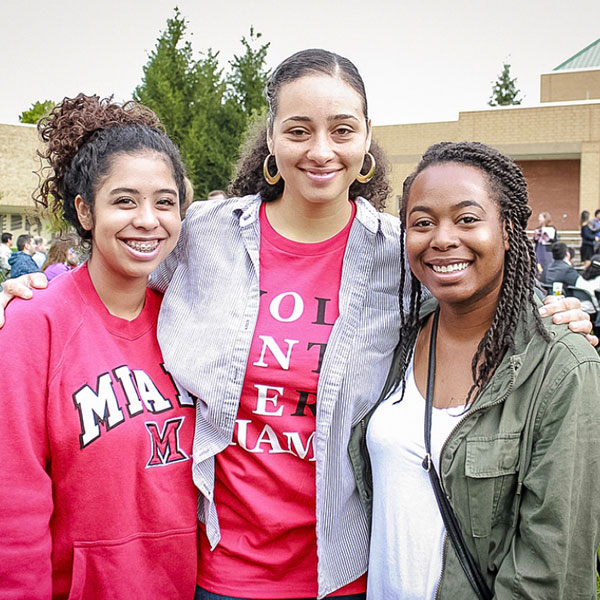 3 women smiling during the Naturalization Ceremony in the Hamilton quad with their arm around each other.