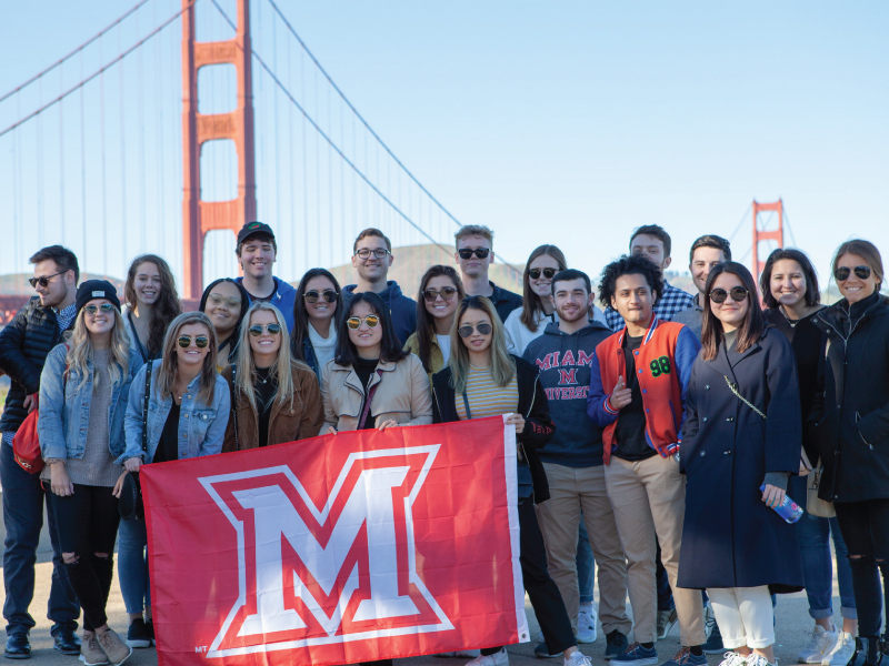 Group of students standing in front of the Golden Gate Bridge in San Francisco holding a Miami M flag.