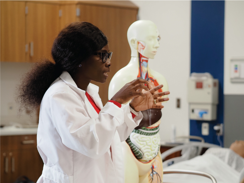 A nursing faculty member standing beside a skeleton model speaking to a class of students