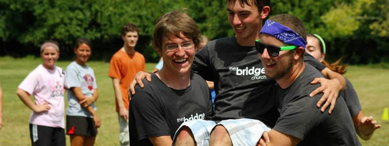 Two students carrying another, laughing, during a Christian student group activity