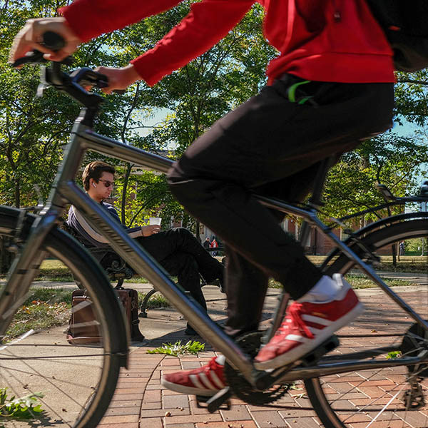 Student walking on campus with a cyclist in the foreground