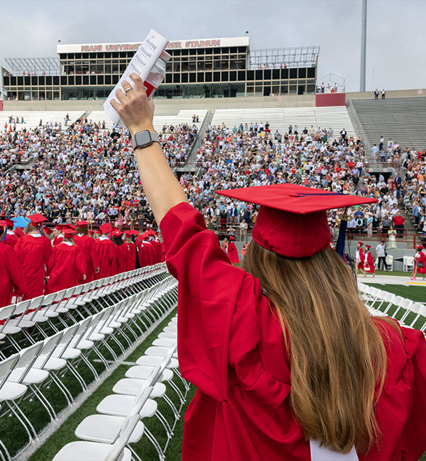 student waving up at the stands at commencement