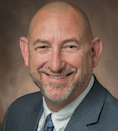 Andy Zeisler wearing a grey suit with a white shirt and blue tie