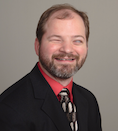 Greg Williams wearing a black suit with red shirt and grey and white tie