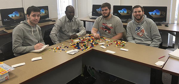 Group of 4 students seated at desks, completing an Agile activity using Lego blocks.