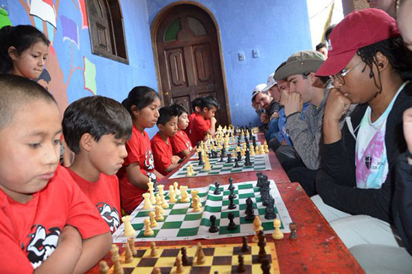 College students playing chess with international children