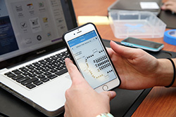 Two hands holding a smart phone in front of a computer screen.