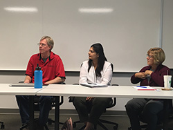 Three people sit at a table listening intently to someone at stage left