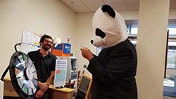 Tony Kinne standing next to a wheel of fortune type wheel and a person in a panda outfit