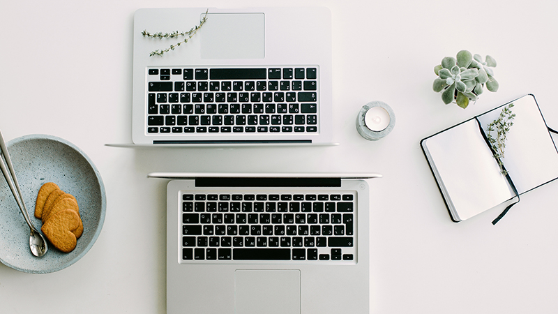 Two computers on a desk with some cookies shaped like hearts on the side