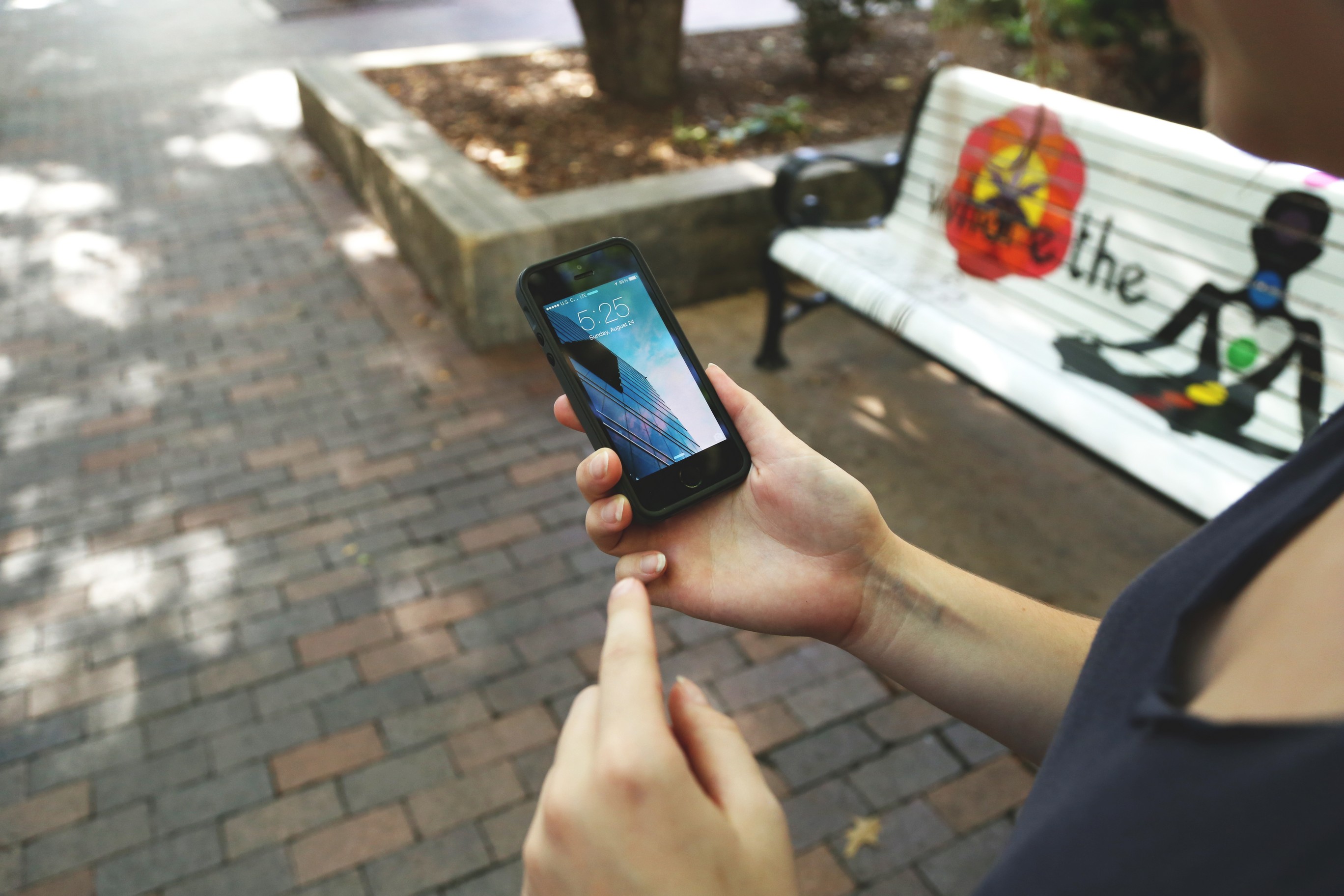 Person holding a cell phone next to a park bench