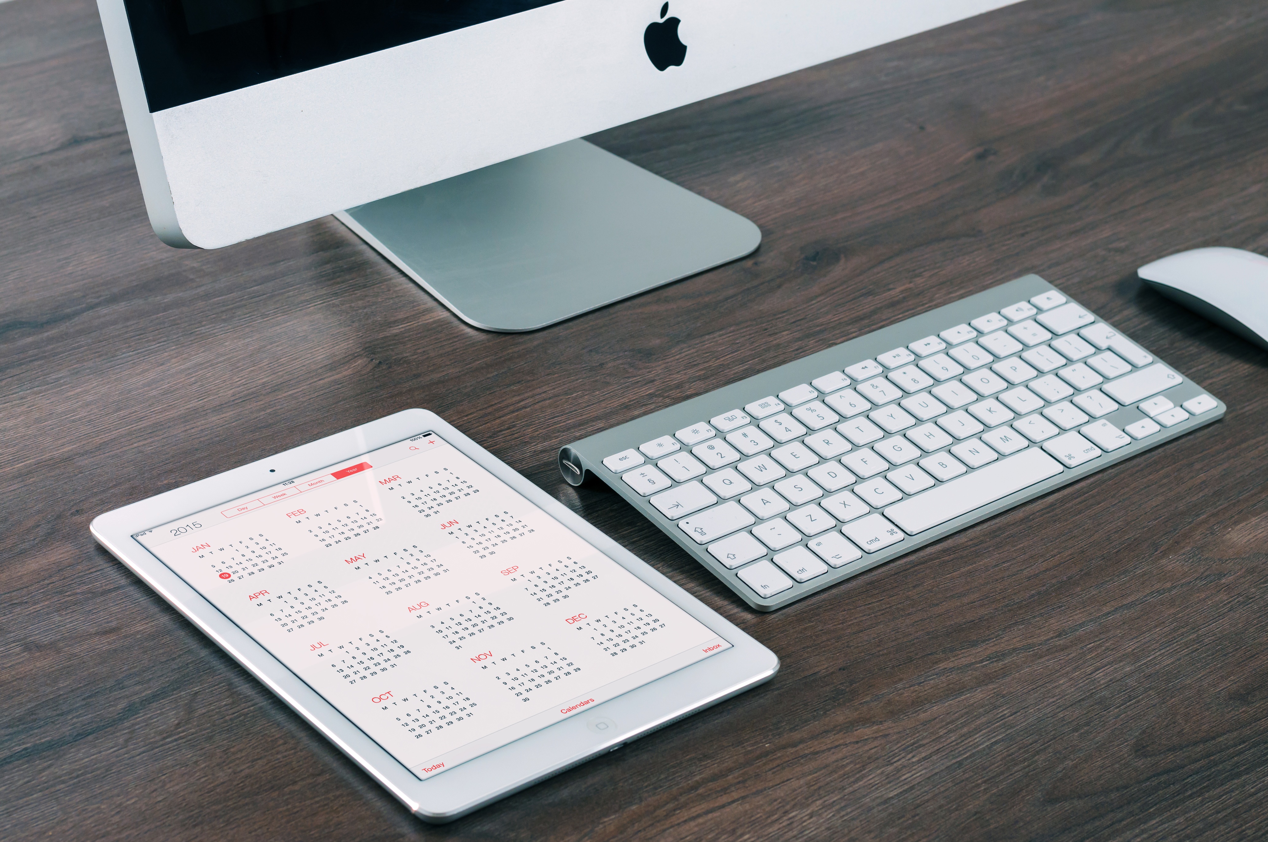 Keyboard, mouse, computer screen and tablet calendar on the top of a desk