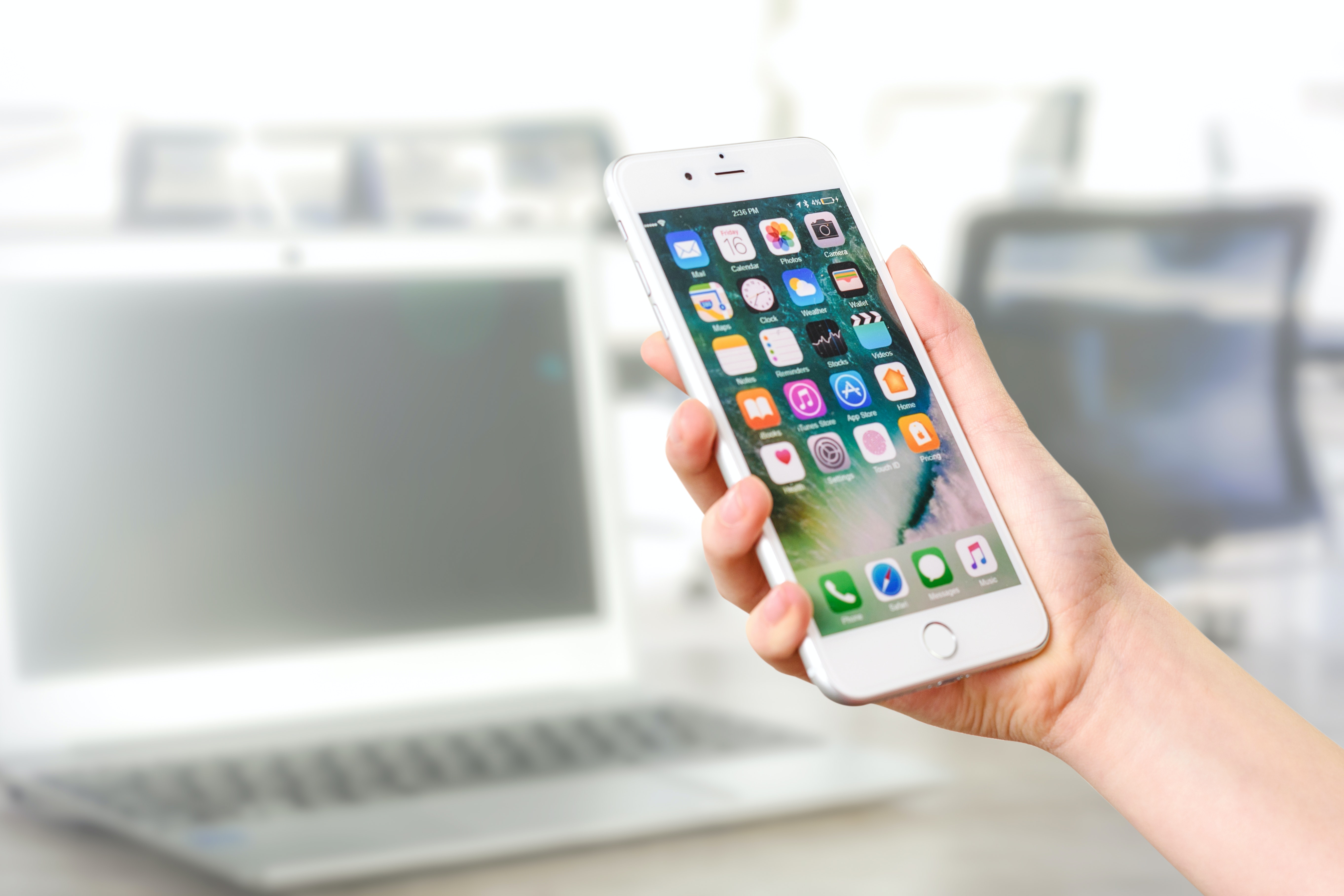 A smartphone behind held by a person. The home screen is unlocked and full of apps