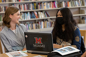 two students wearing masks and sitting at a computer with the red Miami M logo