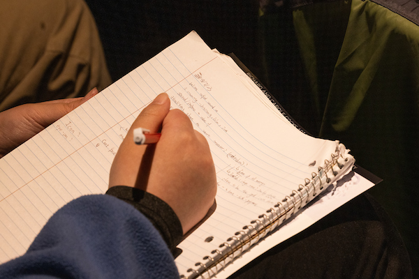 A hand with a pen poised above a notebook, ready to take notes