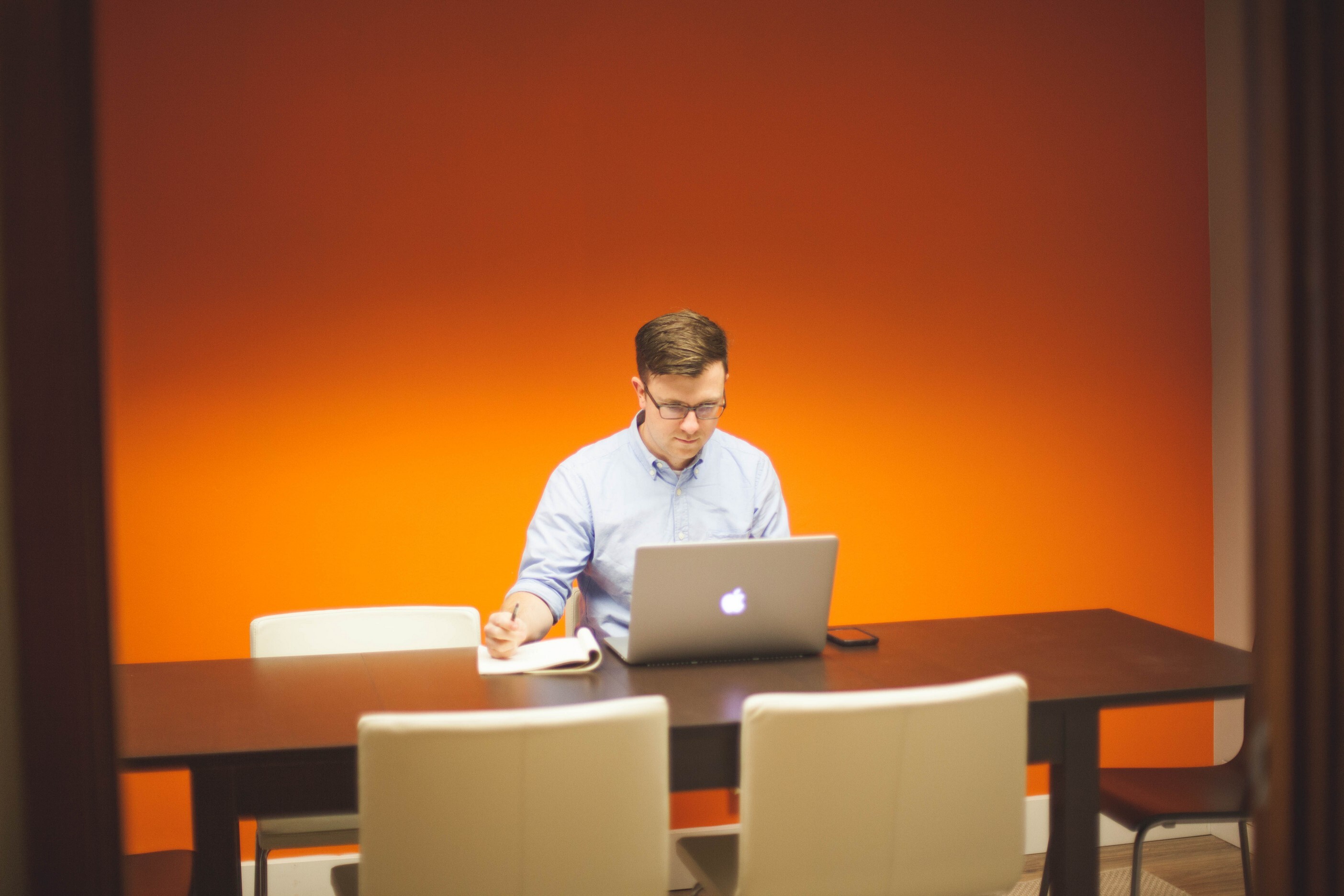 A man sitting at an apple computer in front of an orange wall