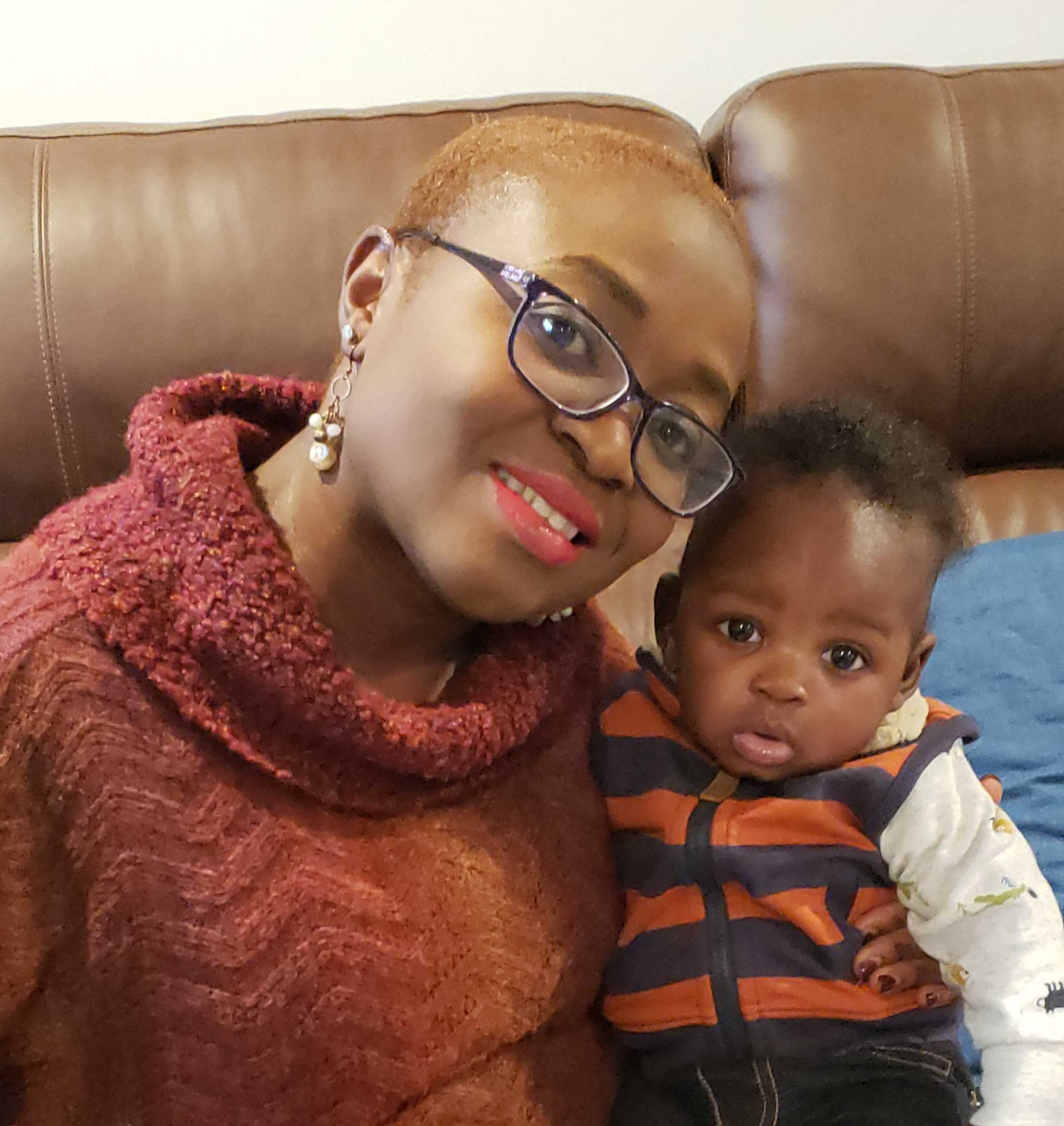 Feminine presenting person holding a baby and smiling at the camera.