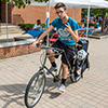 A male student rides a bike while holding up two fingers