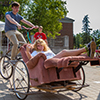 A girl rides in a recliner chair that is attached to a bike driven by a male student