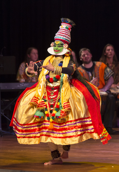 A girl in colorful clothes with her face painted green dances on stage