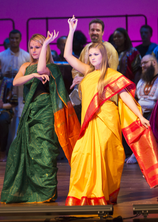 Two females dressed in colorful clothes dance on stage