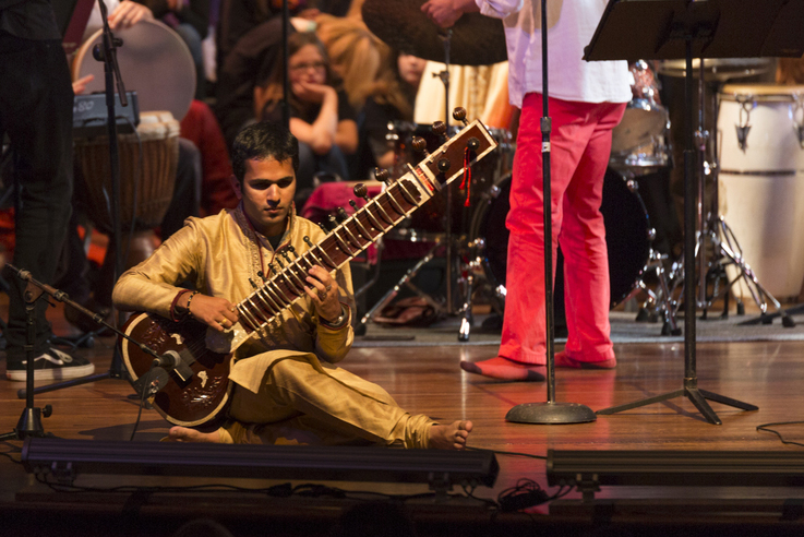 A man sits on the stage while playing a sitar