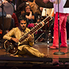 A man sits on the stage while playing a sitar