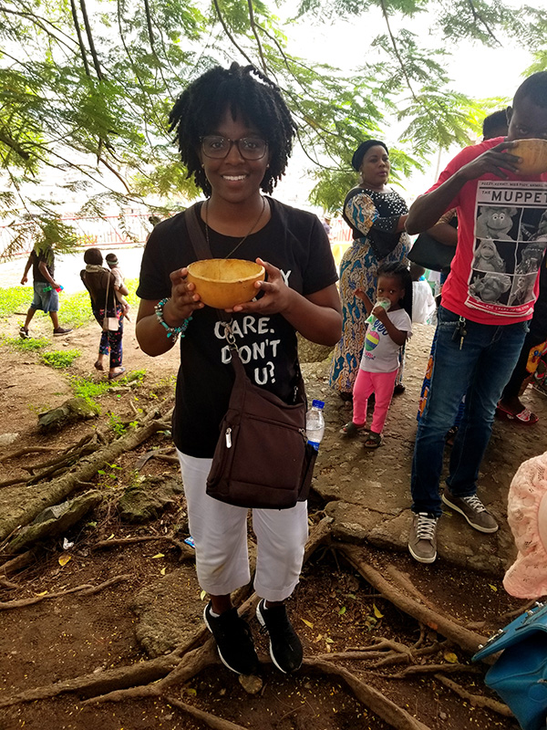 Kala Allen holds a bowl of rice. In the background, several community members are seen going about their day