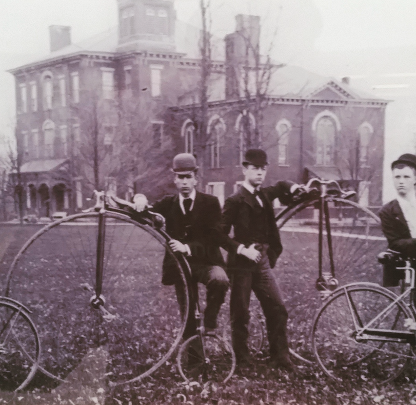 Male students stand near bikes in 1890s.