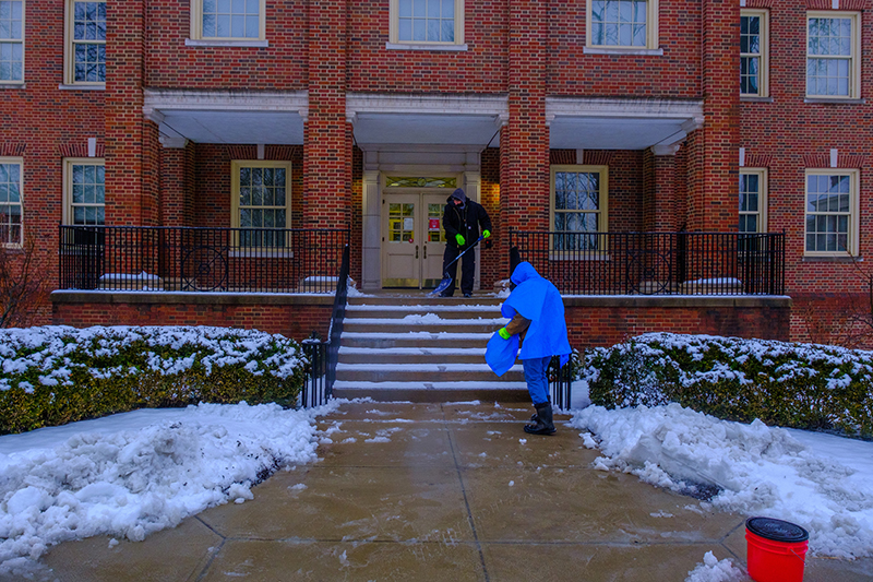 Two Miami employees shovel snow outside of Roudebush Hall