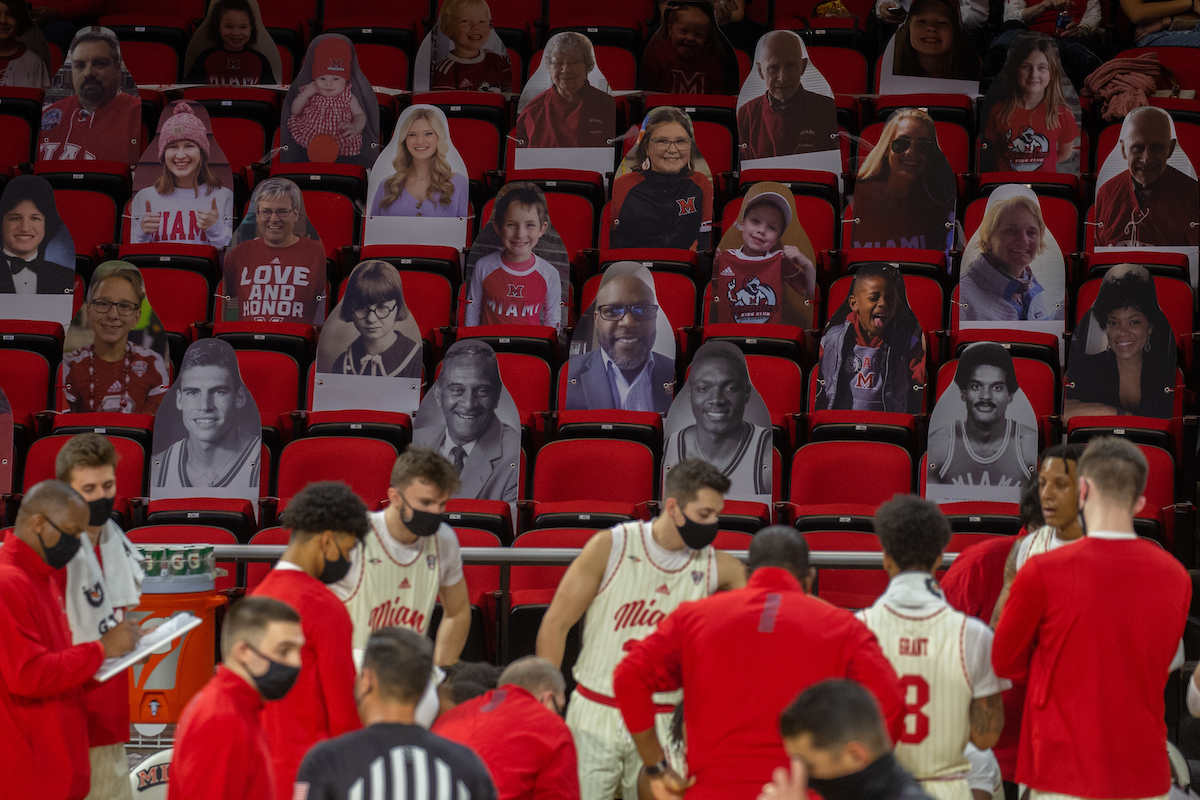 The Miami basketball team huddles in front of a crowd of 2D cutout fans