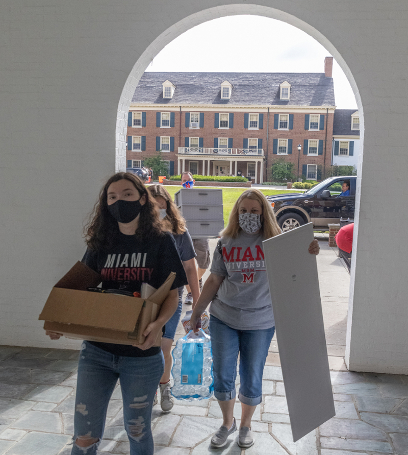 three people carry boxes in morris hall through archway framing a view of tappan hall