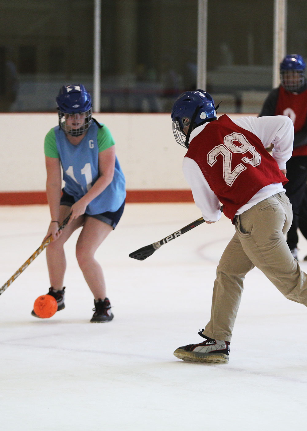 Two students play broomball on opposing teams, one student is protecting the goal