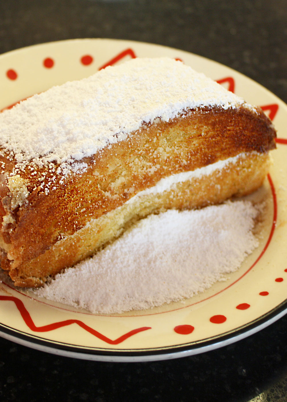 A toasted Tuffy's roll on a plate, dusted with powdered sugar