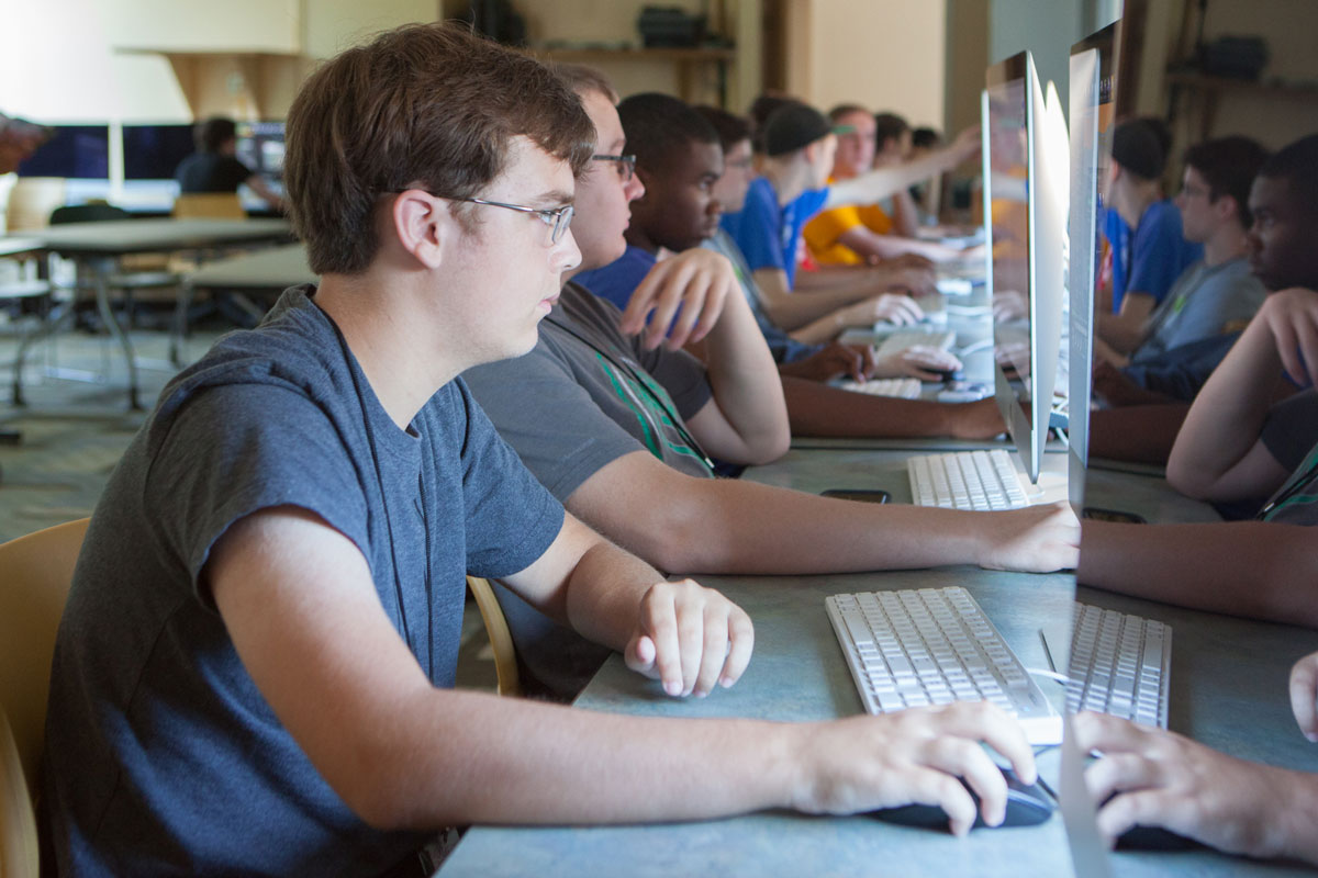 A young male-presenting person sits at a desk in front of a computer