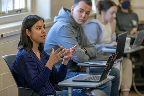 Miami student explains conversing with the rest of her class who are seated at desks with open laptops